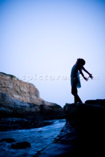 Silhouetted portrait of Stephanie Crocker with her arms back like wings standing on a rock over the ocean. Santa Cruz, California.