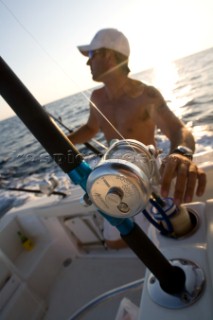 A fisherman rigging a line on a fishing pole as the sun flares behind him in Cocos Island, Costa Rica.