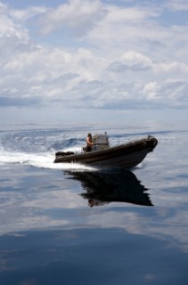 An inflatable zodiac glides through the water, reflected in its surface along with the with the clouds overhead in Costa Rica.