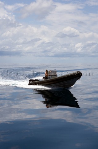 An inflatable zodiac glides through the water reflected in its surface along with the with the cloud