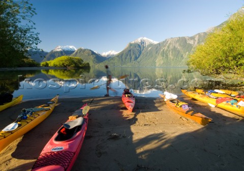 Ben Sanders walks past a group of kayaks while holding a paddle in Lago Yelcho Chile