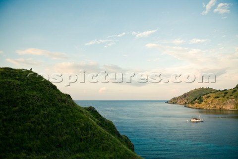 A man sits on the lush green grass covered hillside overlooking his boat in the bay of a small islan