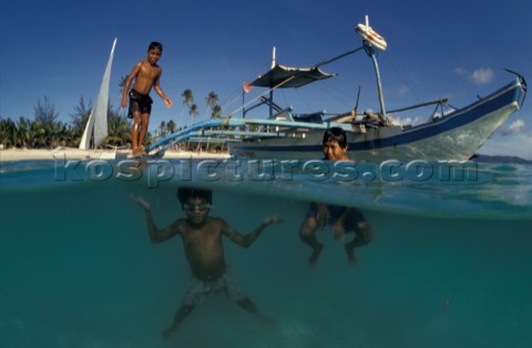 Filipino boys swim from off an outrigger boat anchored on shore Boracay Philippines