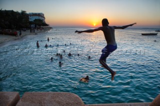 An unidentified boy jumps in the sea as the sun goes down  in the old stone town in Zanzibar Town, Zanzibar, Tanzania. The island has a long history with slave trade and was ruled by Omani Arabs during the early 19th century. The Island is predominately Muslim and has become a popular tourist destination in recent years. The Island is a two-hour boat ride from Dar Es Salaam, Tanzania on the east African coast. The island is part of Tanzania.