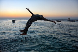 An unidentified boy jumps in the sea as the sun goes down  in the old stone town in Zanzibar Town, Zanzibar, Tanzania. The island has a long history with slave trade and was ruled by Omani Arabs during the early 19th century. The Island is predominately Muslim and has become a popular tourist destination in recent years. The Island is a two-hour boat ride from Dar Es Salaam, Tanzania on the east African coast. The island is part of Tanzania.