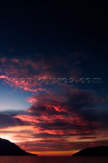 Sunrise over the Adriatic Sea in January. Red clouds lit by the sunlight and the island on the right side of the photo. Shot in Budva, Montenegro.