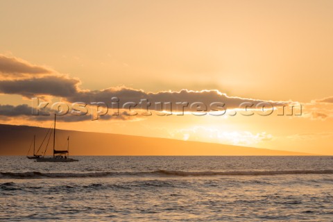 A sailboat at sunset with an island in the distance off the coast of Maui